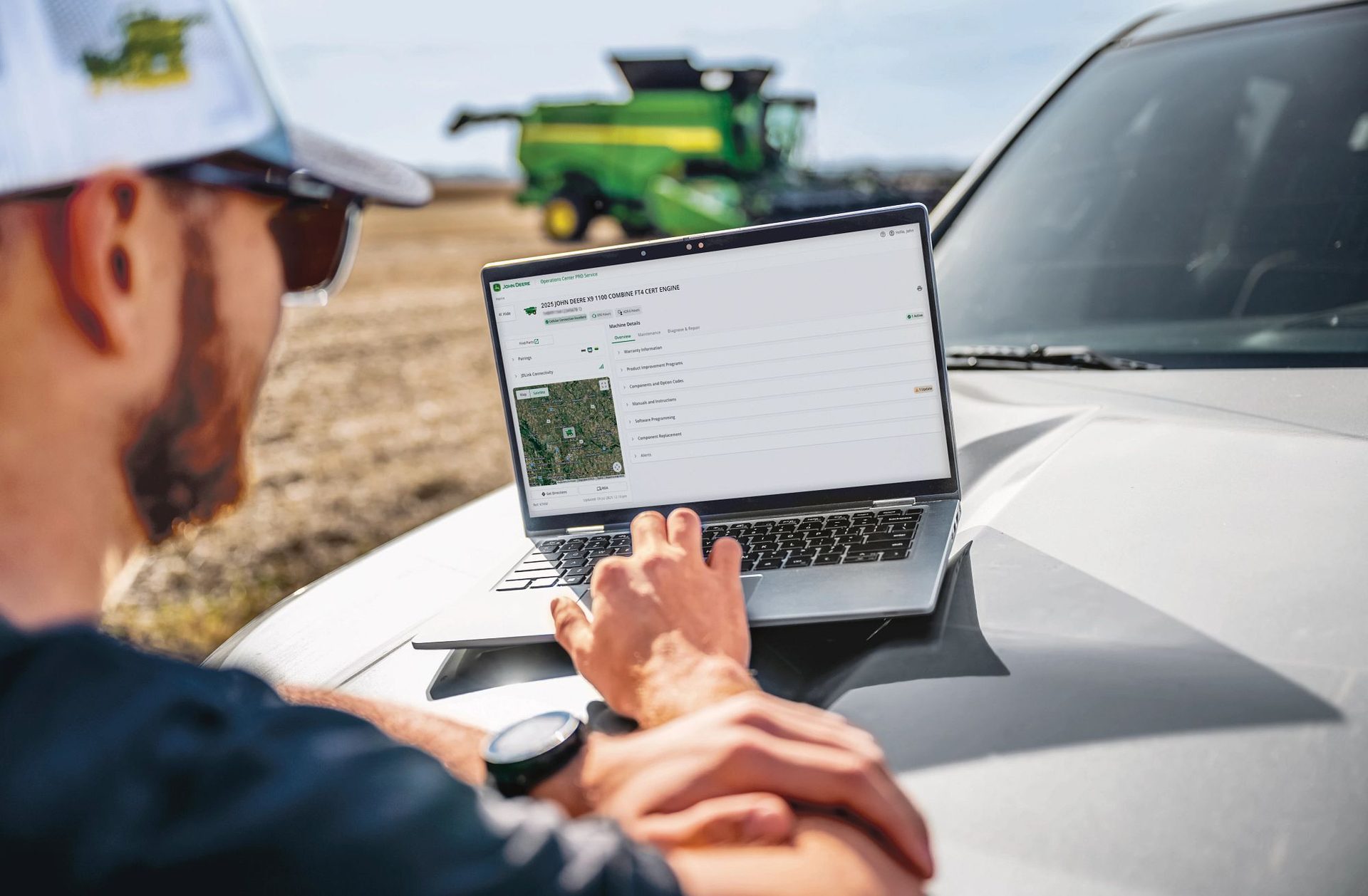 Farmer reviewing John Deere Operations Center on a laptop in a field with a combine behind him