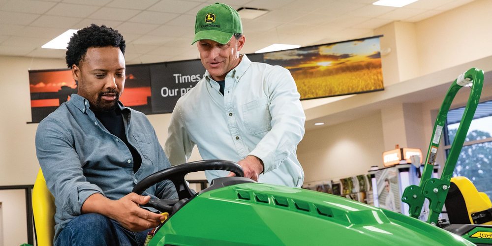 Salesperson showing a customer a new John Deere lawn tractor in the showroom