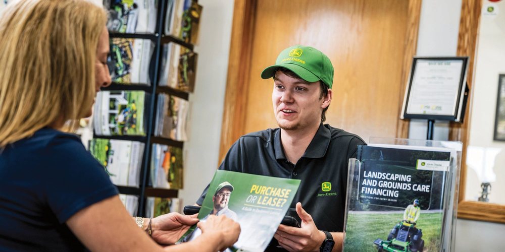 Salesperson reviewing a John Deere landscaping and grounds care financing brochure with a customer