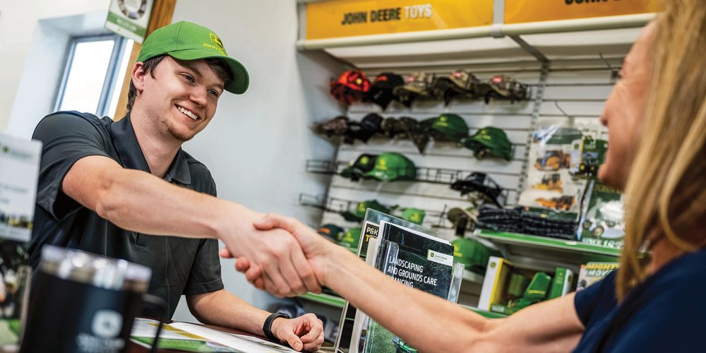 Dealer and customer shaking hands at the sales counter after a John Deere purchase