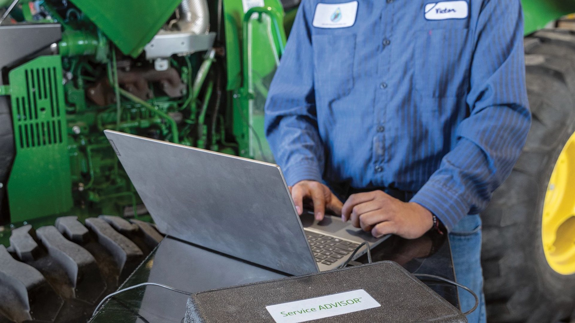 Technician running John Deere Service ADVISOR diagnostics on a laptop connected to a tractor