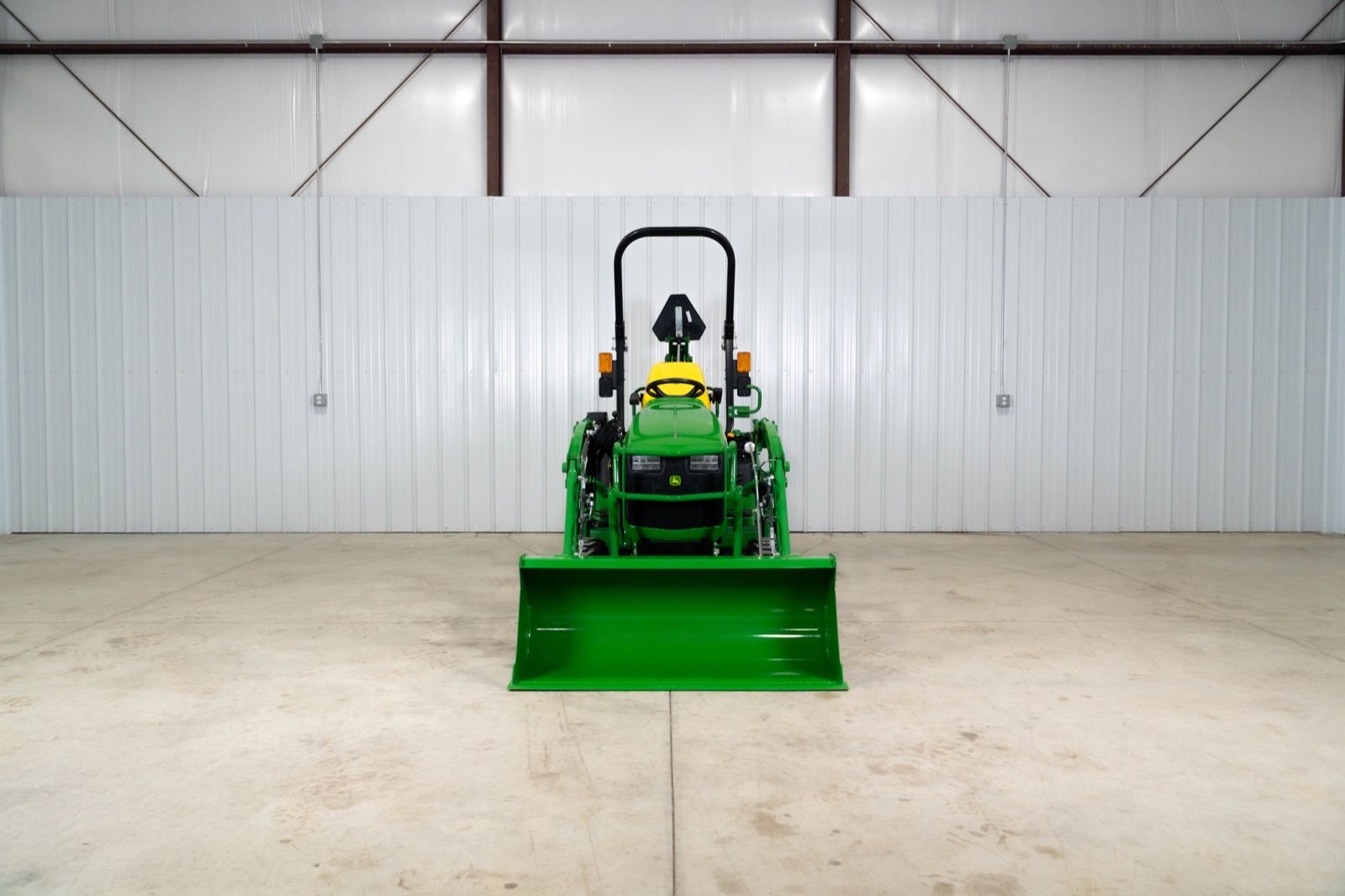 Front view of John Deere 1025R tractor with 120R loader and bucket, parked indoors