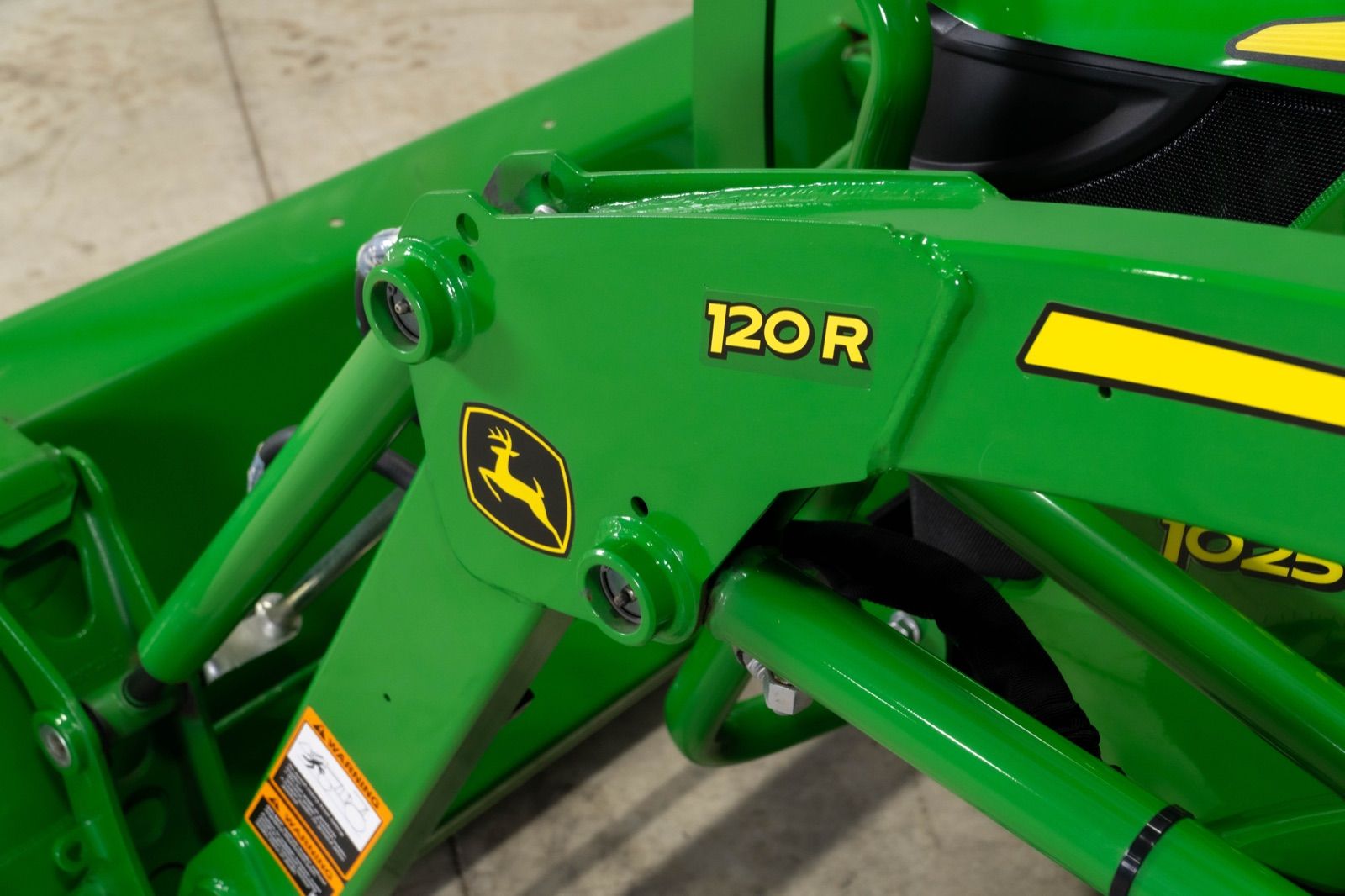 Close-up of the green 120R loader arm with John Deere logo and hydraulic components