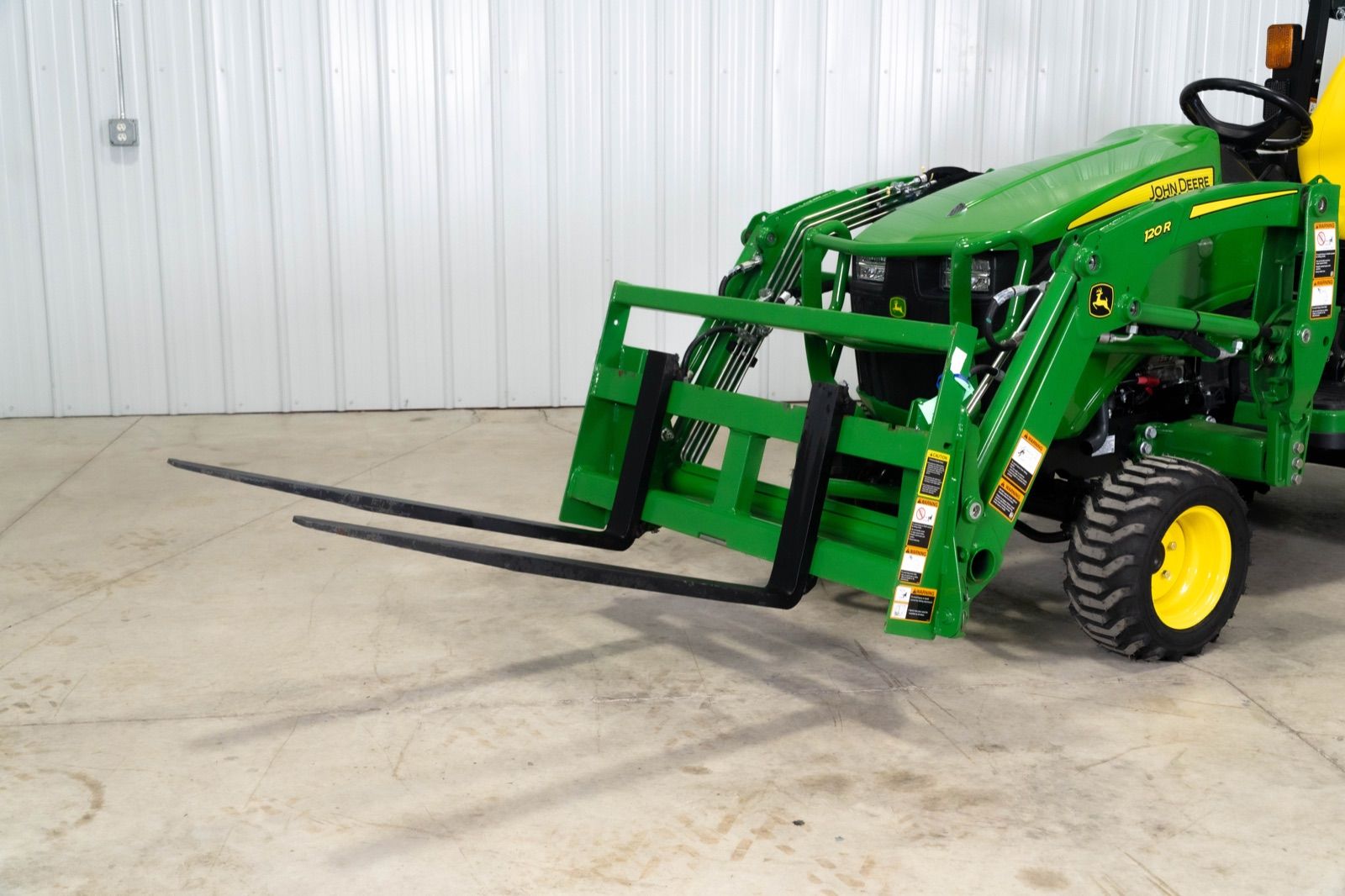 John Deere 1025R tractor with AP11F pallet forks attached to the 120R loader, indoors
