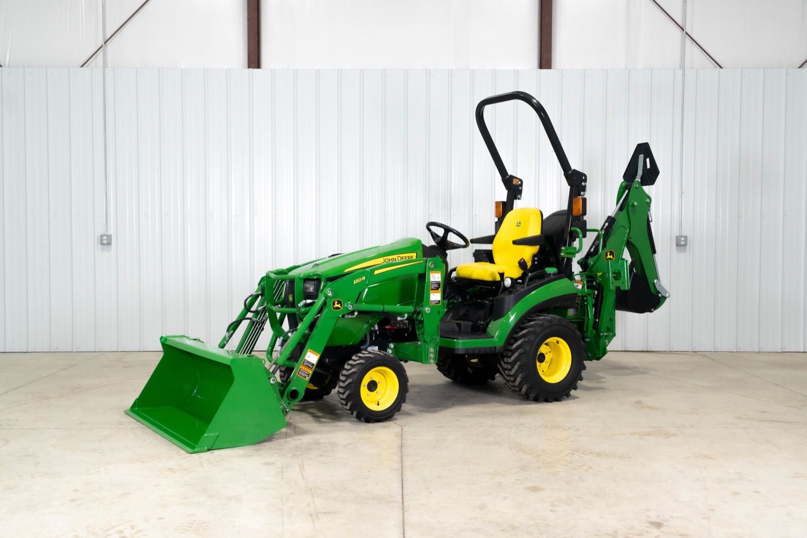 John Deere 1025R tractor with 120R loader and bucket, and 260B backhoe, parked indoors