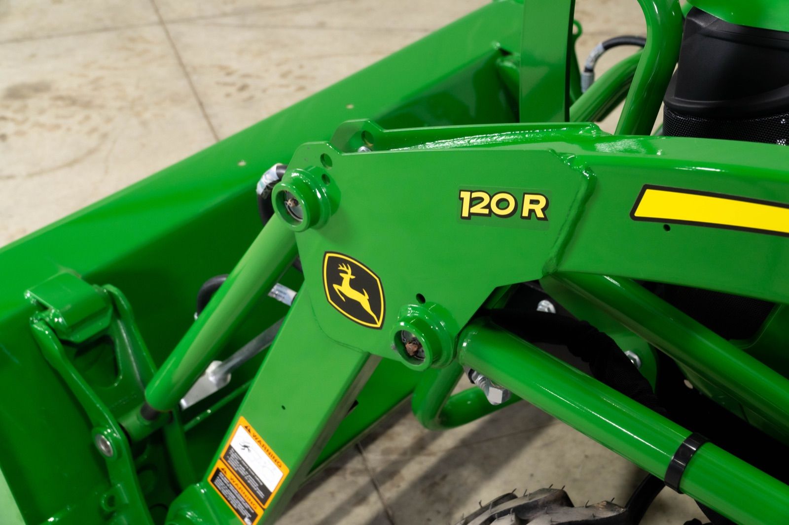 Close-up view of the green 120R loader arm on the John Deere 2025R tractor, showing model number