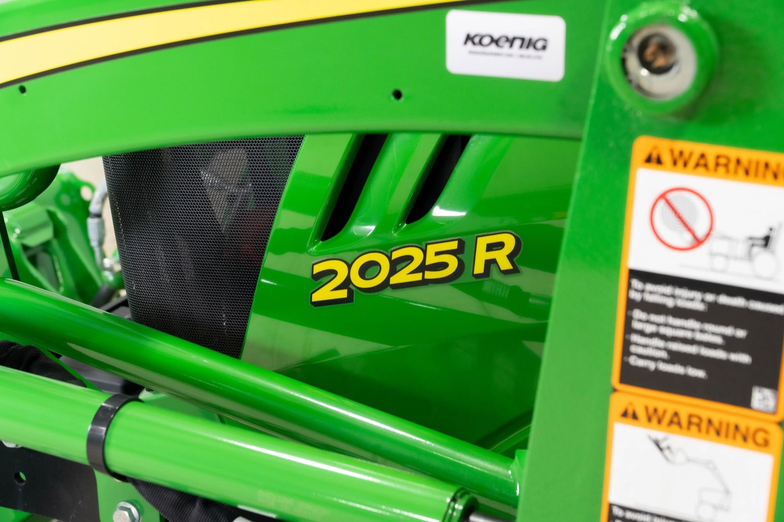 Close-up of the hood of the John Deere 2025R tractor, showing '2025 R' model number and warning label