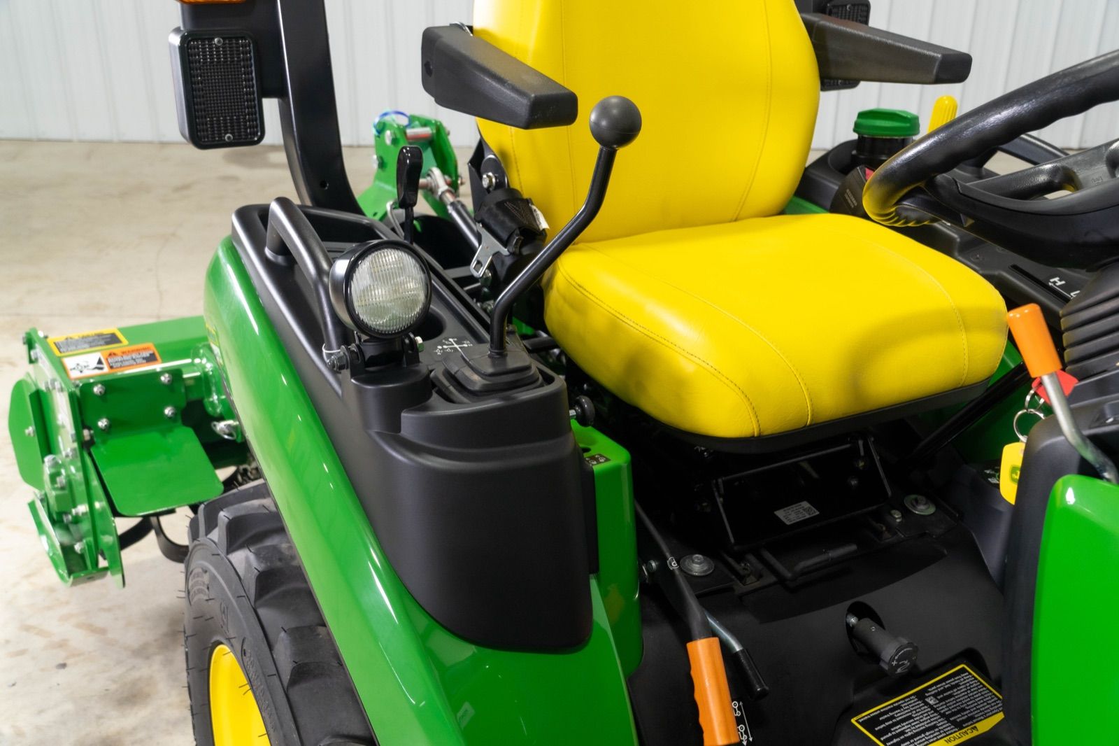 Operator station of the John Deere 2025R tractor, showing the yellow seat and control levers