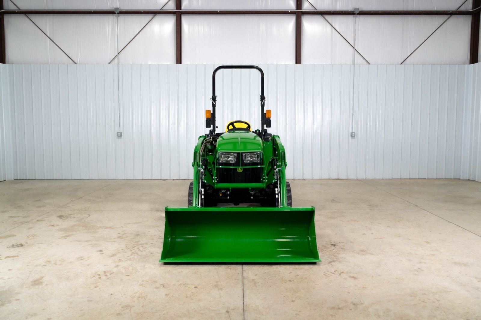 John Deere 3038E tractor with a green 300E loader and bucket attached, parked in a white garage