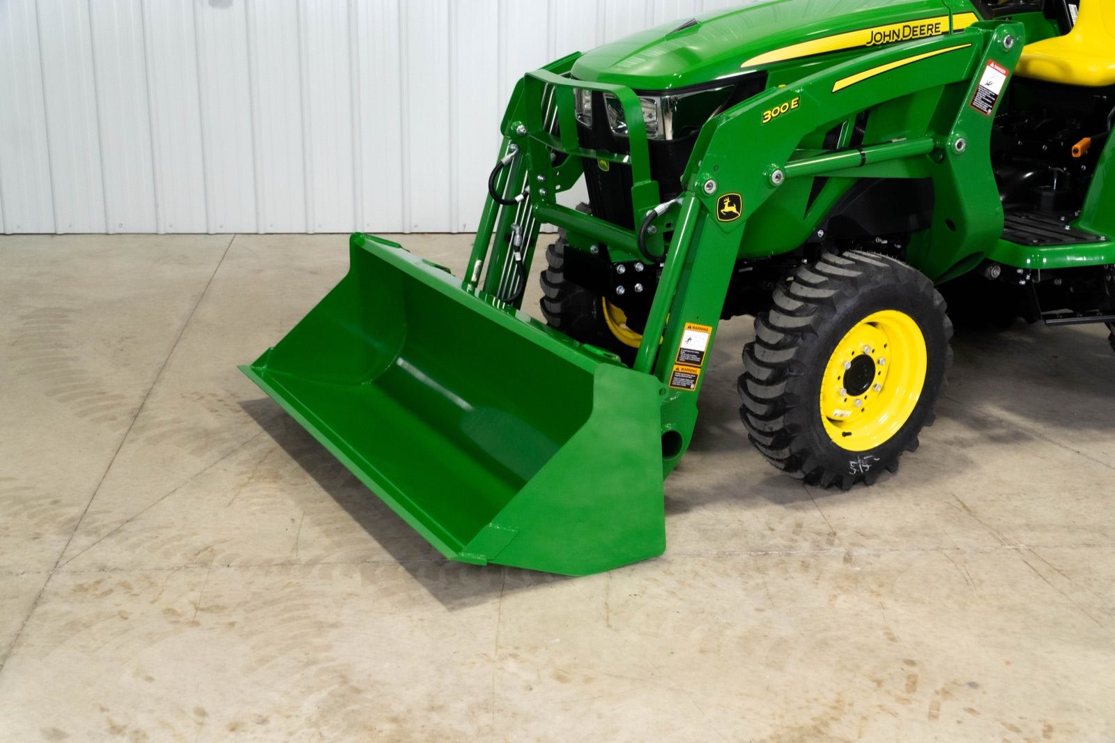 Close-up of the green 300E loader and bucket attached to the front of the John Deere 3038E tractor