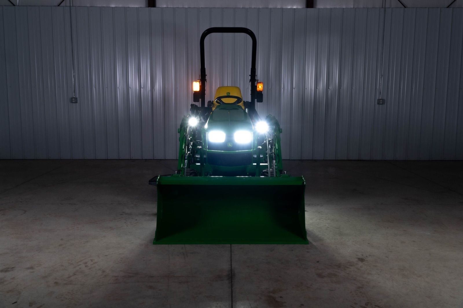 Front view of John Deere 1025R tractor with 120R loader and bucket, headlights illuminated
